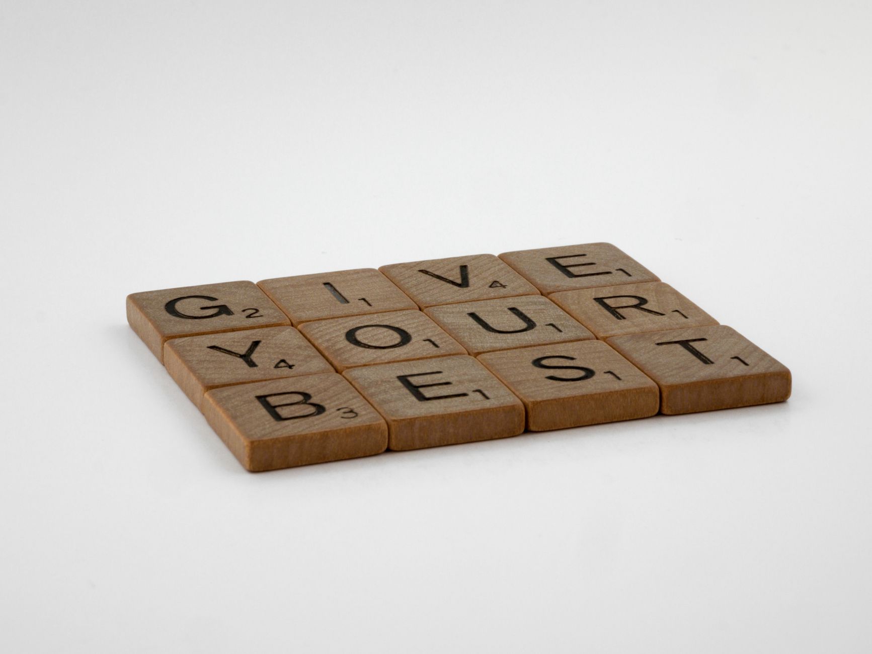 Wooden scrabble tiles arranged to spell 'Give Your Best' on a simple background.